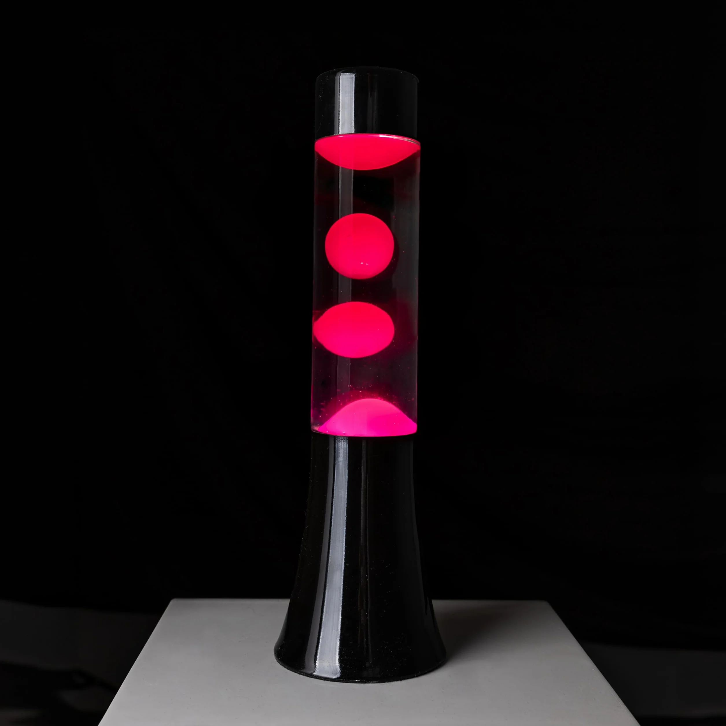 Fisura - Różowa lampa lawa. Lampa lawa o wysokości 30 cm z czarną podstawą, różową lawą i przezroczystym płynem. Relaksująca lampa. 9x9x30 cm
