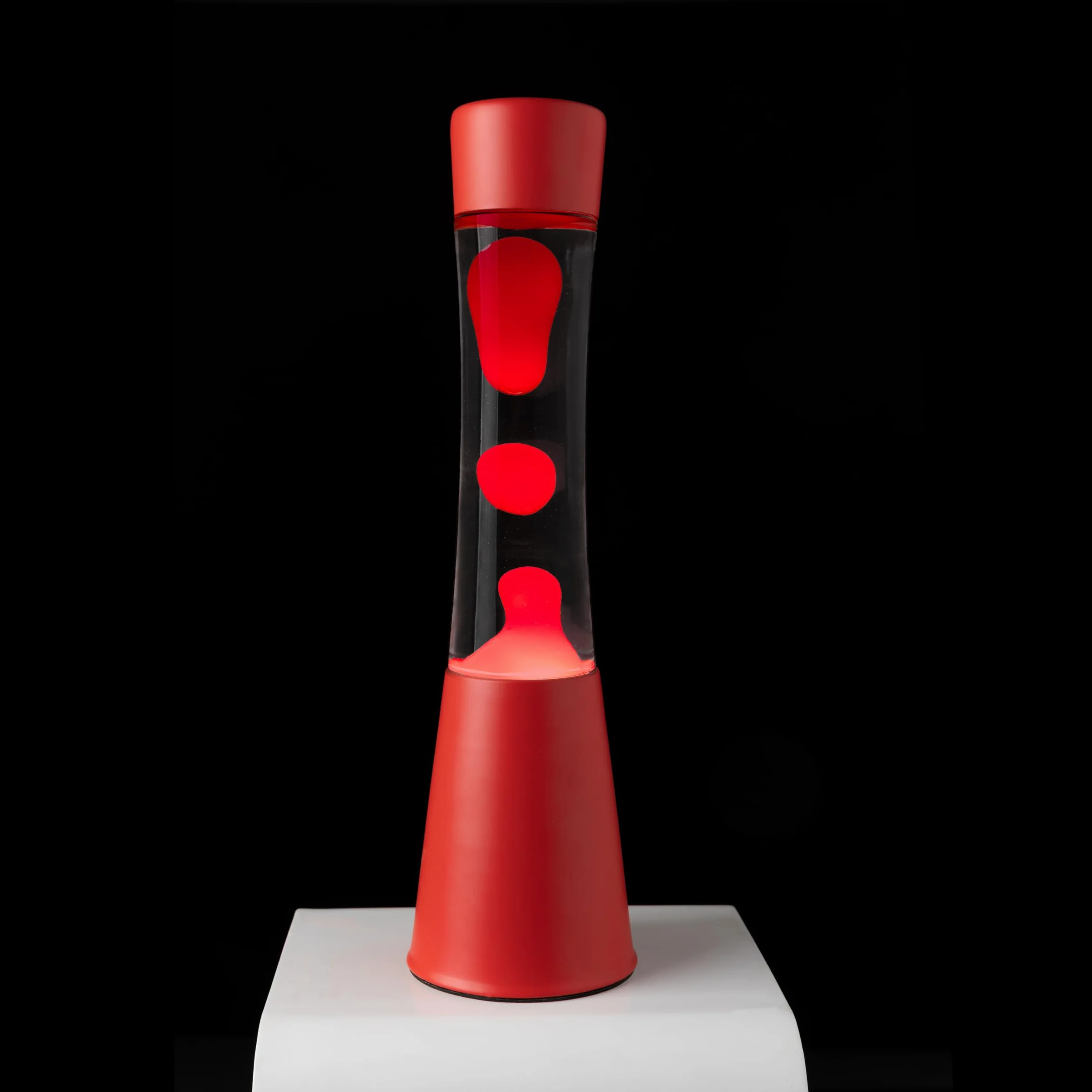 Fisura – Lampa z lawą czerwona. Podstawa i lawa w kolorze czerwonym z przezroczystym płynem. Lampa relaksacyjna z zapasową żarówką. 11 cm x 11 cm x 39,5 cm.